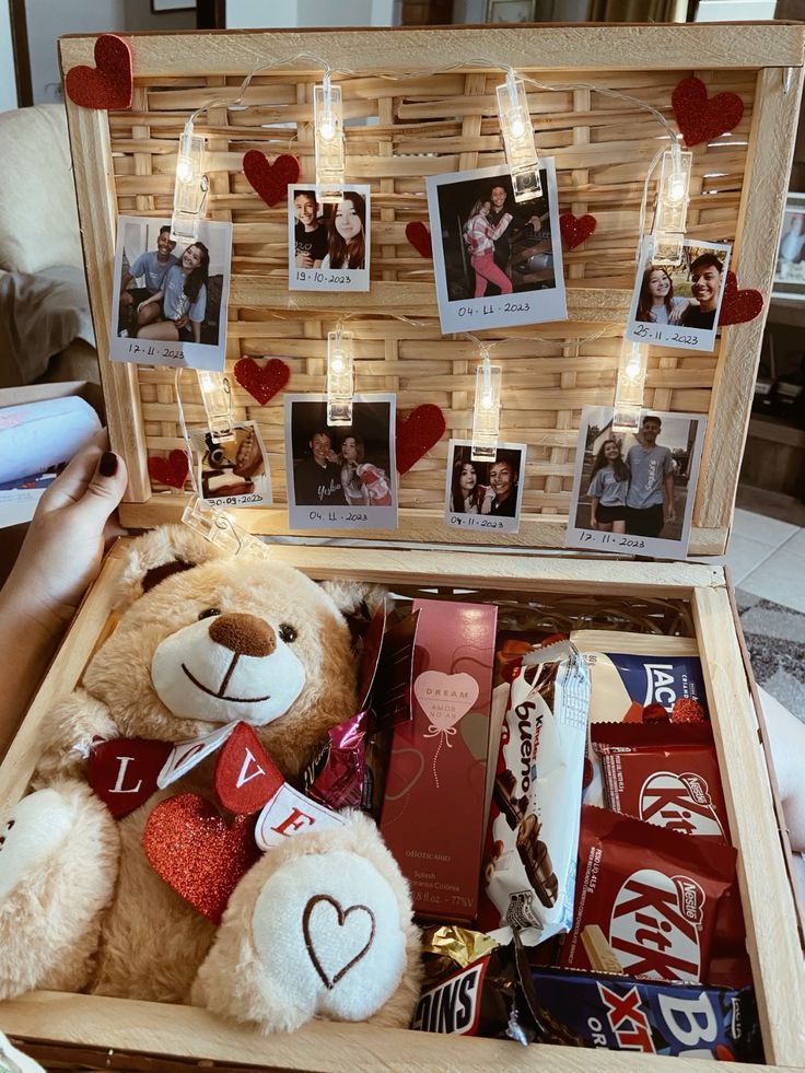 Gift box with teddy bear, snacks, chocolates, and love-themed decorations, featuring hung photos with string lights.