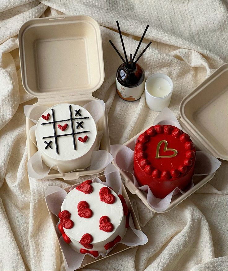 Decorative cakes with heart designs in eco-friendly boxes on a fabric background, accompanied by a candle and diffuser.