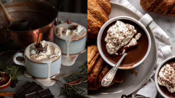 Two mugs of hot chocolate with whipped cream and cinnamon sticks, surrounded by croissants and festive decor.