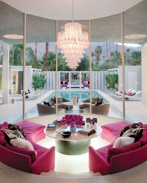 Luxurious living room with vibrant pink sofas, modern chandelier, and pool view through large windows.