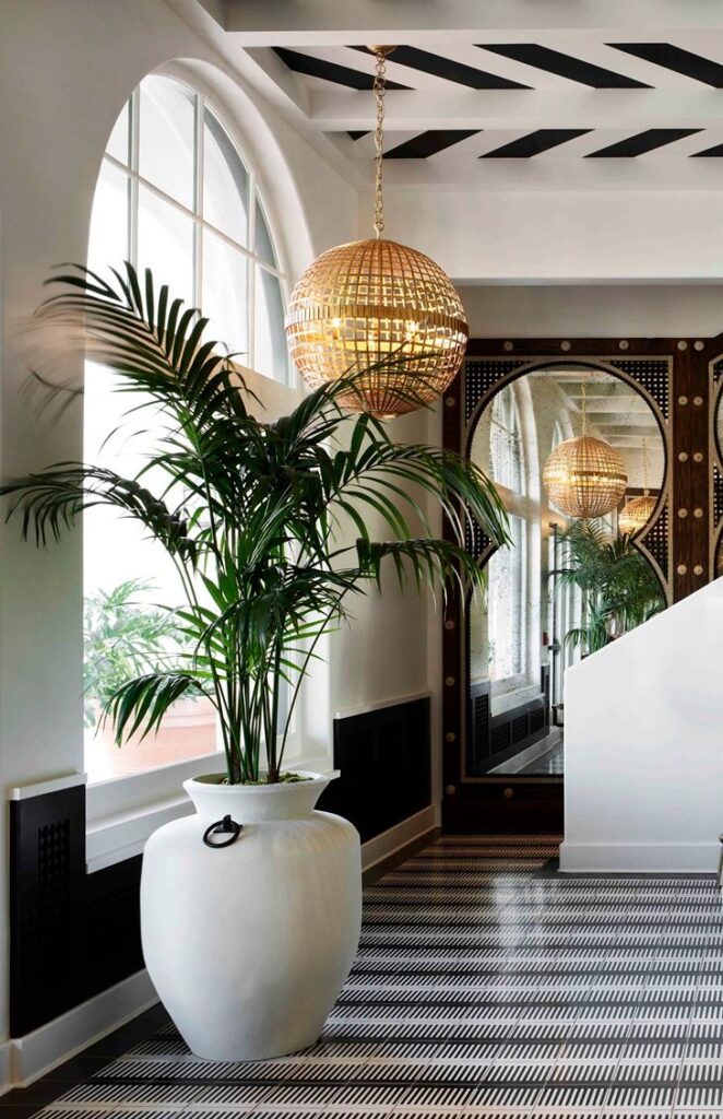 Elegant hallway with palm plant in white vase, gold spherical pendant light, and large decorative mirror.