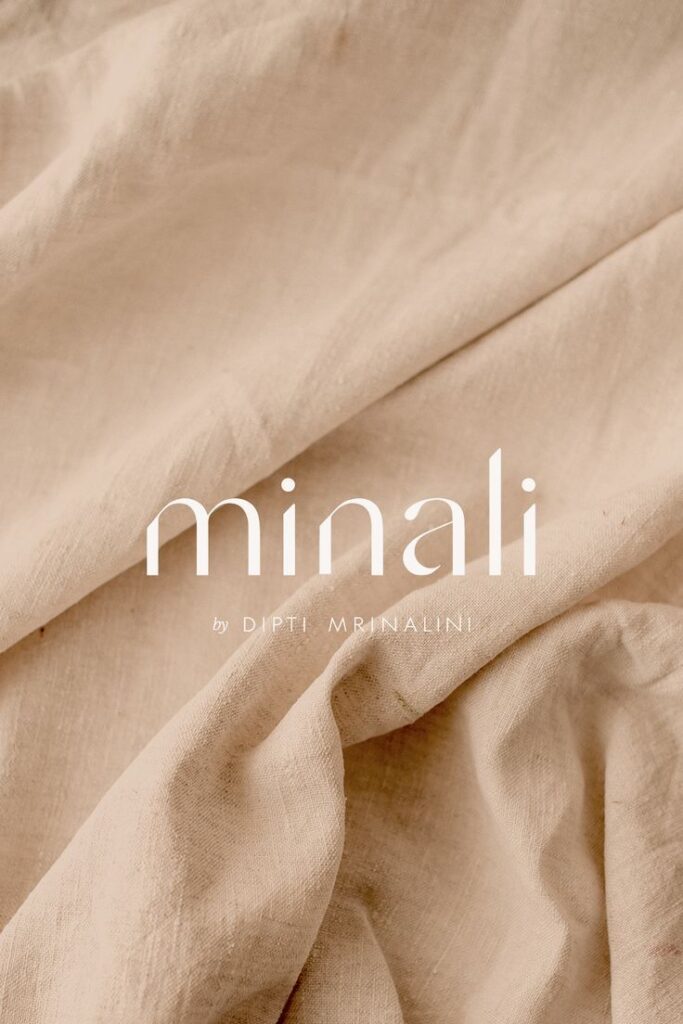 Soft beige fabric with 'minali by Dipti Mrinalini' text overlay, showcasing natural textile texture and elegance.