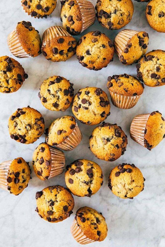 Chocolate chip muffins scattered on a white marble surface. Freshly baked and golden brown treats.