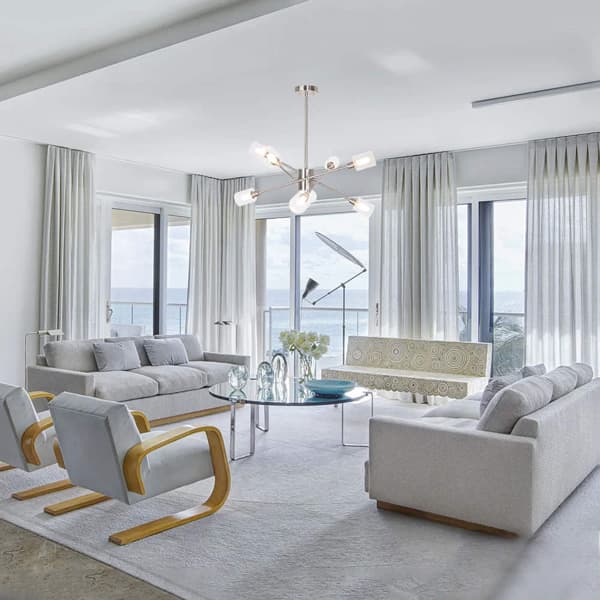 Modern living room with ocean view, elegant furniture, and contemporary lighting. Neutral tones and large windows.