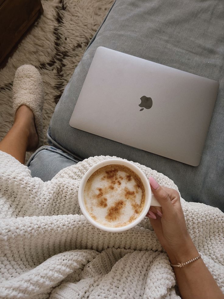 Cozy morning with coffee, laptop, and comfy blanket on couch, creating a perfect relaxing work-from-home atmosphere.