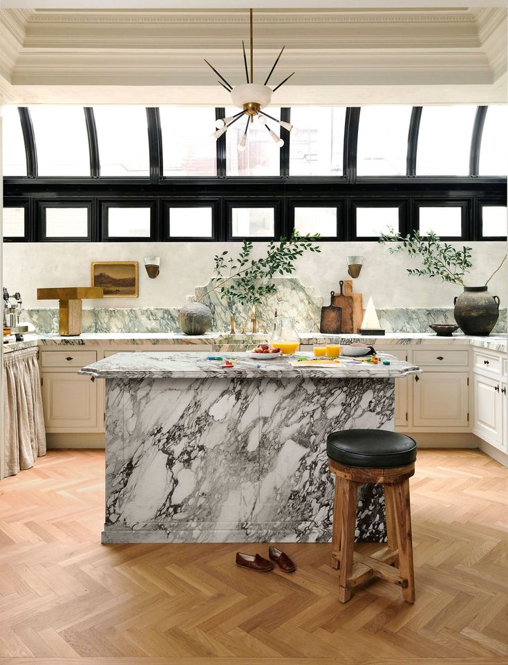 Modern kitchen with marble island, parquet flooring, elegant lighting, and natural light from arched windows.