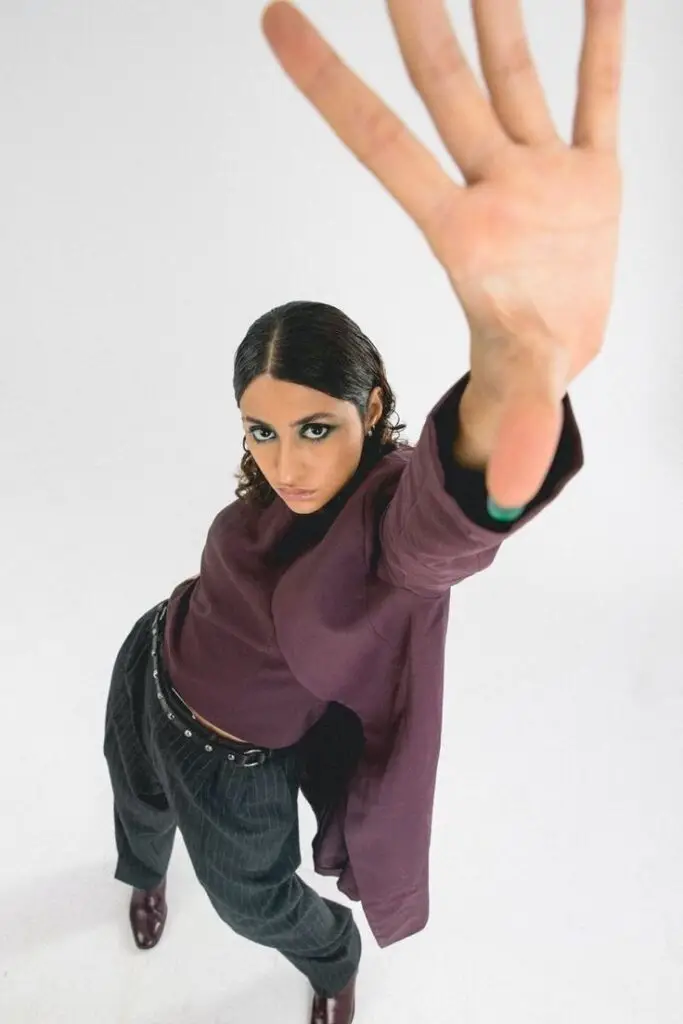 Woman in stylish maroon outfit poses dynamically, reaching towards the camera on a white background.