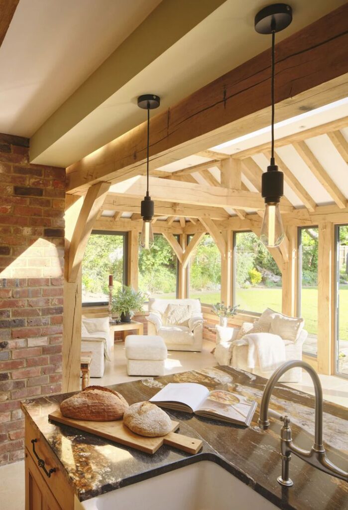 A cozy sunlit kitchen with rustic wooden beams, open layout, and fresh bread on a marble countertop.