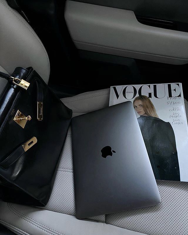 Laptop, fashion magazine, and luxury handbag on a car seat, combining technology and style essentials for modern professionals.