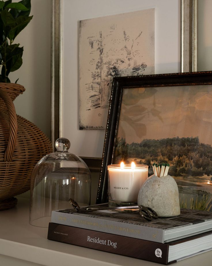 Cozy home decor with lit candle, art prints, and books on a shelf, creating a warm and inviting atmosphere.