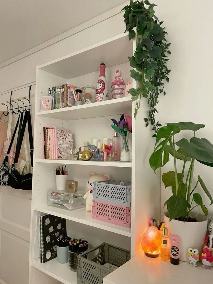 White shelf with plants, books, cosmetics, and decor in a neatly organized room. Cozy and stylish interior setup.