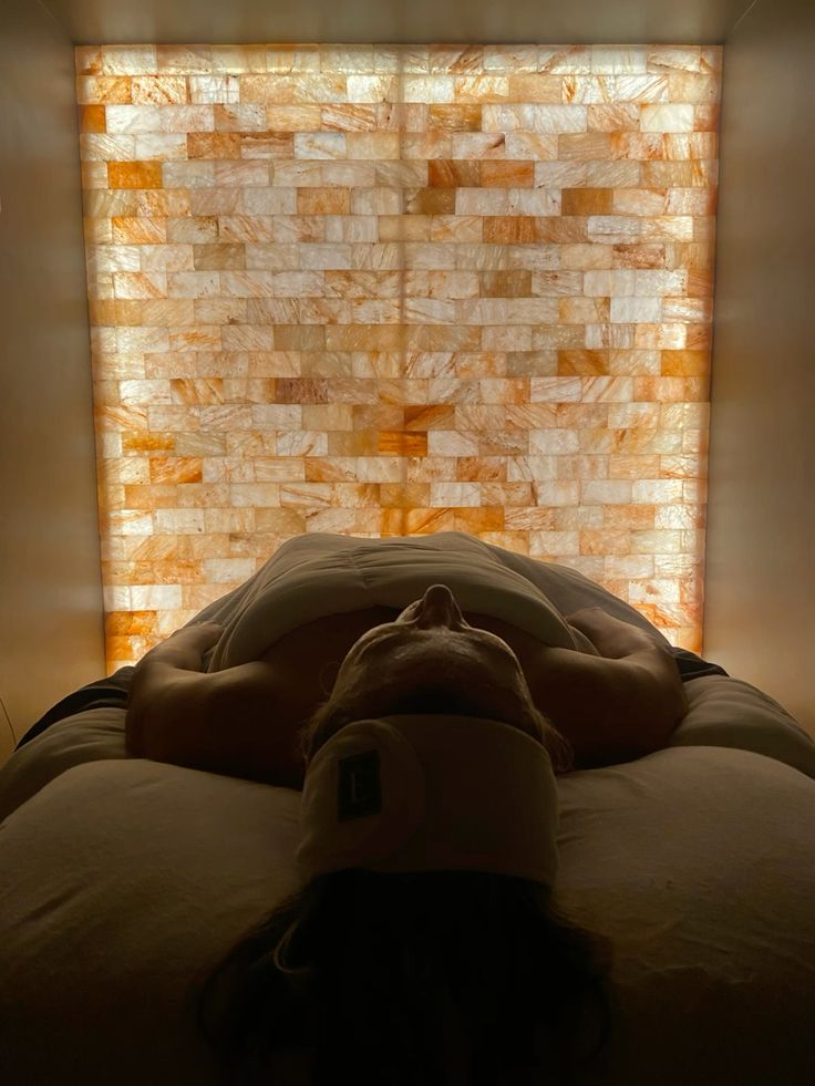 Person relaxing in a salt room, halo therapy spa experience with warm backlit salt wall, promoting wellness and calm.