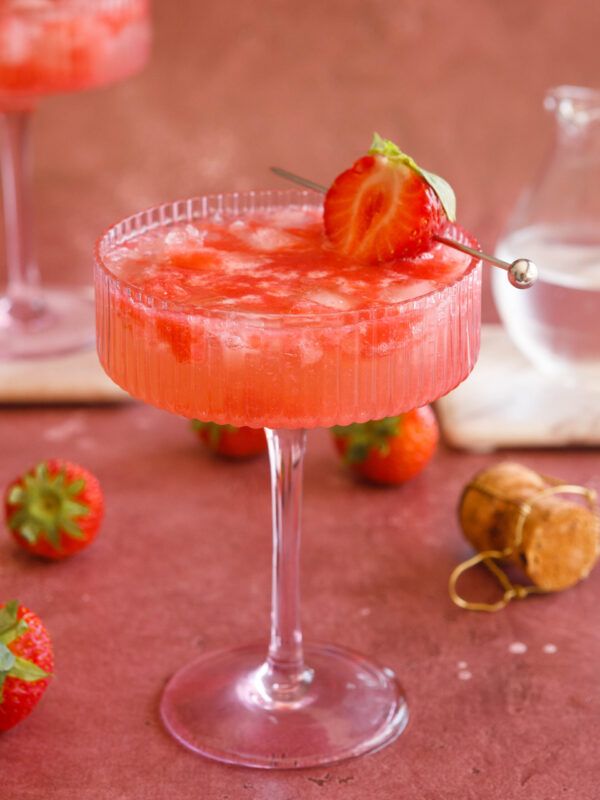 Chilled strawberry cocktail in a glass, garnished with fresh strawberry on a pink background.