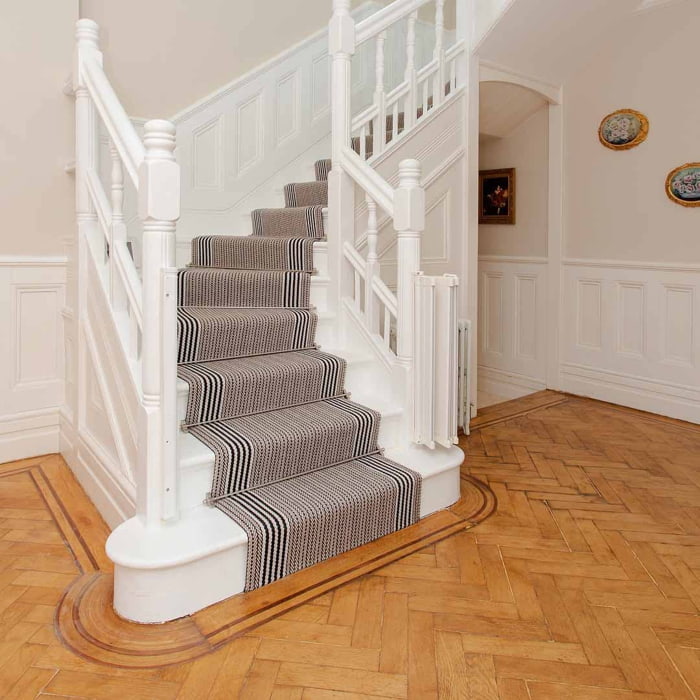 Elegant staircase with striped carpet runner and white banister, leading to the second floor in a stylish home interior.