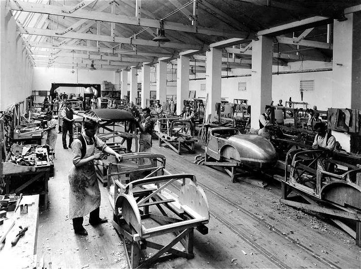 Historic car factory with workers assembling vehicles on a production line.