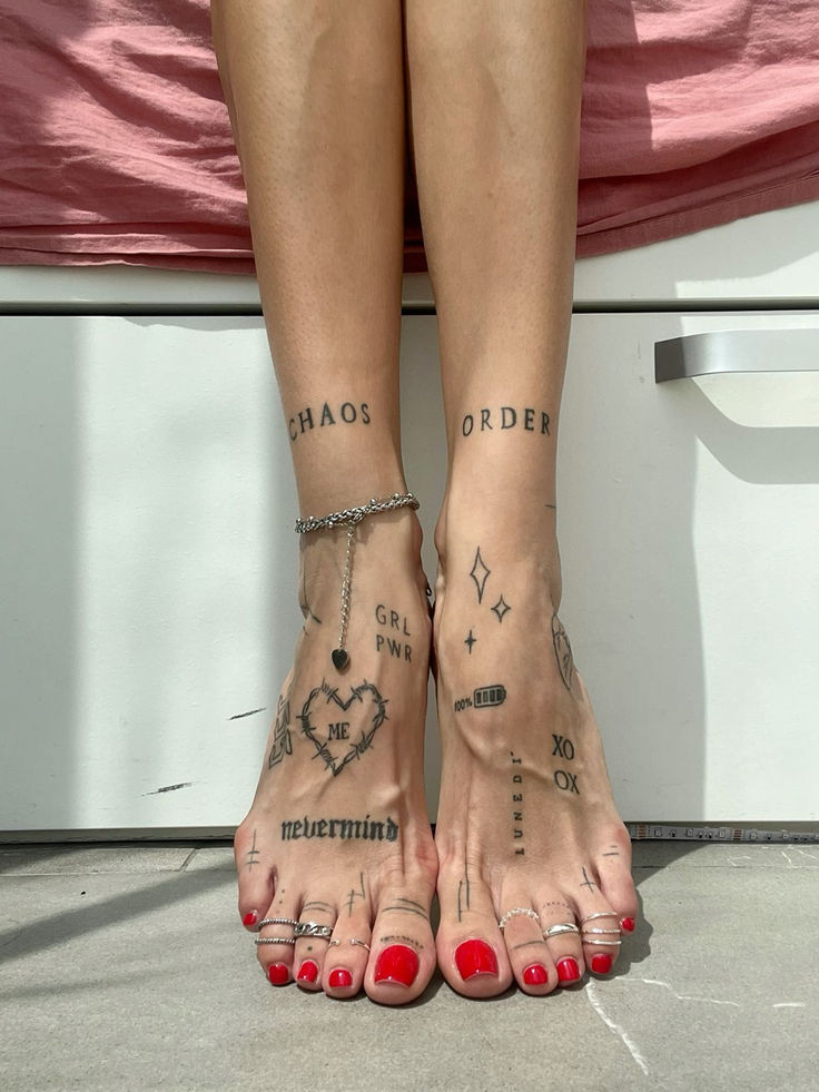 Feet with tattoos and red nail polish, featuring words and symbols like Chaos and Order, against a minimalist backdrop.