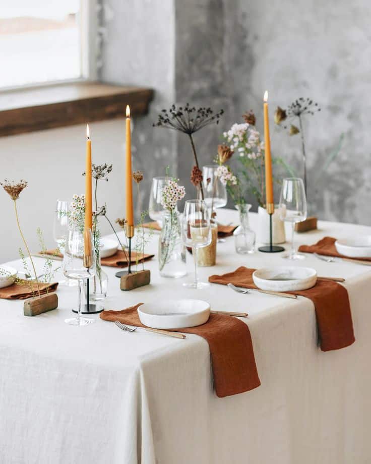 Elegant dining table setup with candles, flowers, and brown napkins, creating a cozy and sophisticated atmosphere.