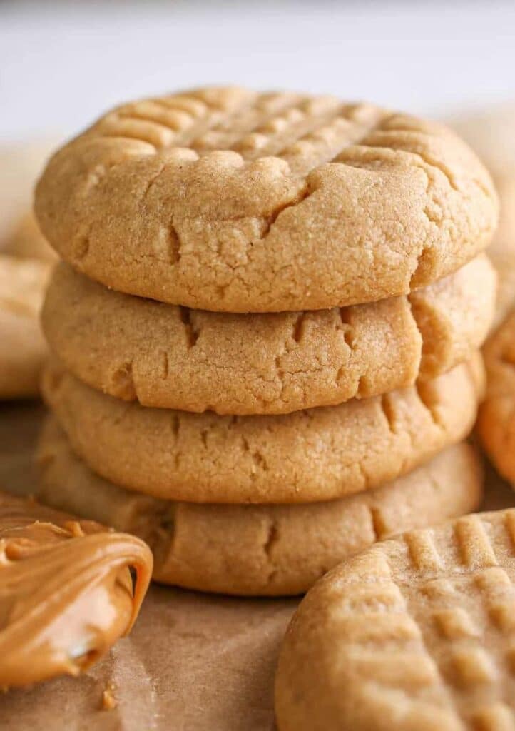 Stack of homemade peanut butter cookies on a wooden table, with a dollop of creamy peanut butter beside them.