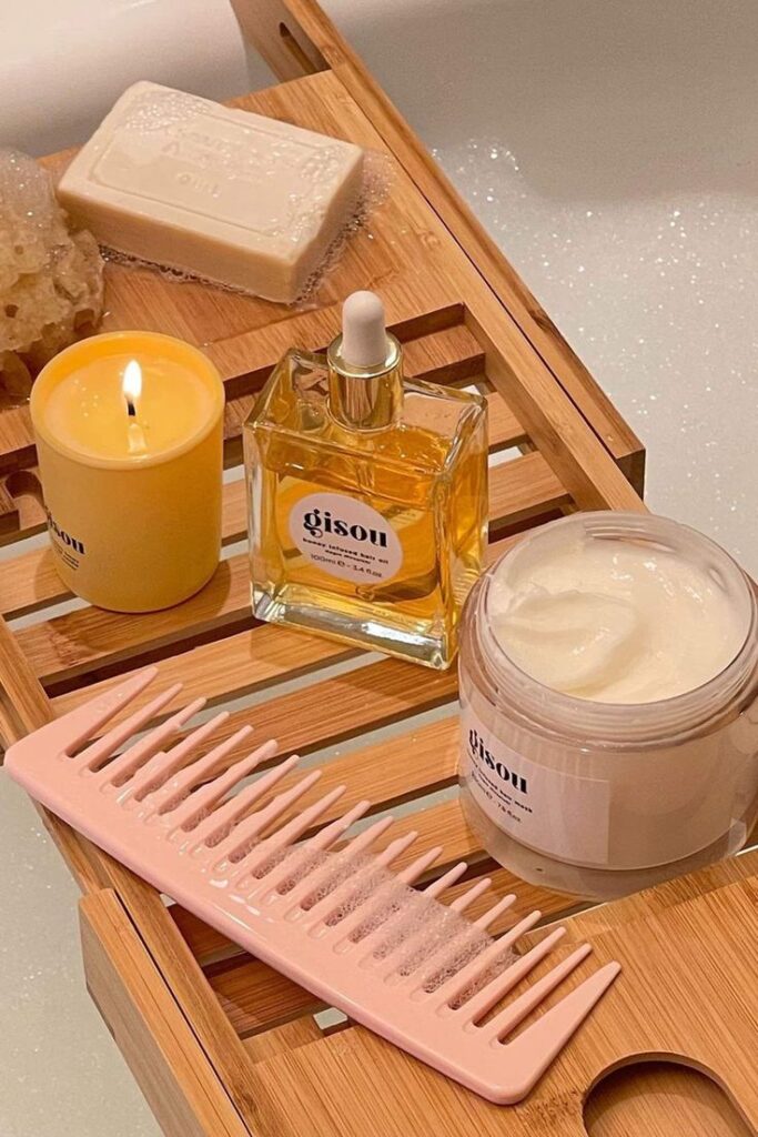 Relaxing bath essentials: candle, hair oil, cream, soap, comb on a wooden tray for a serene spa experience.