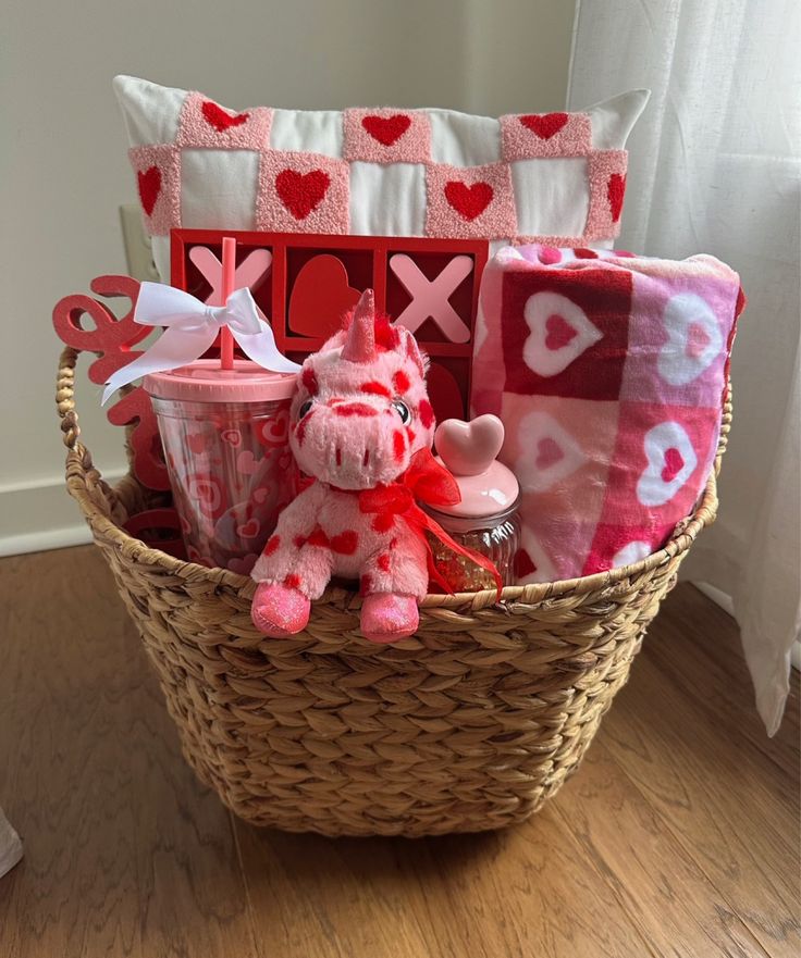 Gift basket with heart-themed items: pillow, plush unicorn, blanket, tumbler, and tic-tac-toe game. Perfect for Valentine's Day.