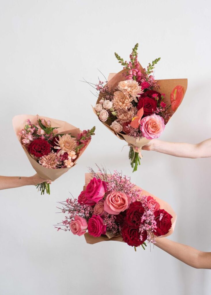 Three vibrant flower bouquets with red, pink, and peach roses held against a white background. Perfect for celebrations.