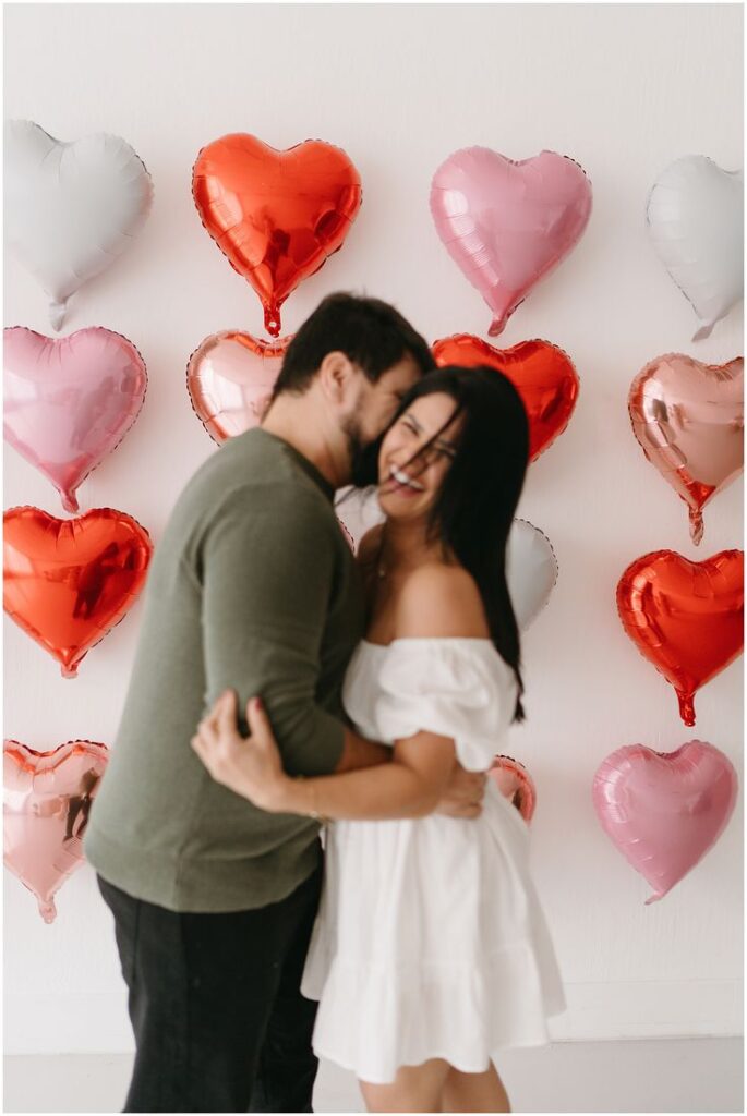 Couple laughing and embracing in front of heart-shaped balloons, symbolizing love and joy.