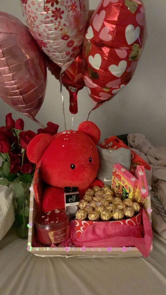 Valentine's gift basket with red teddy bear, chocolates, candy, and heart-shaped balloons.