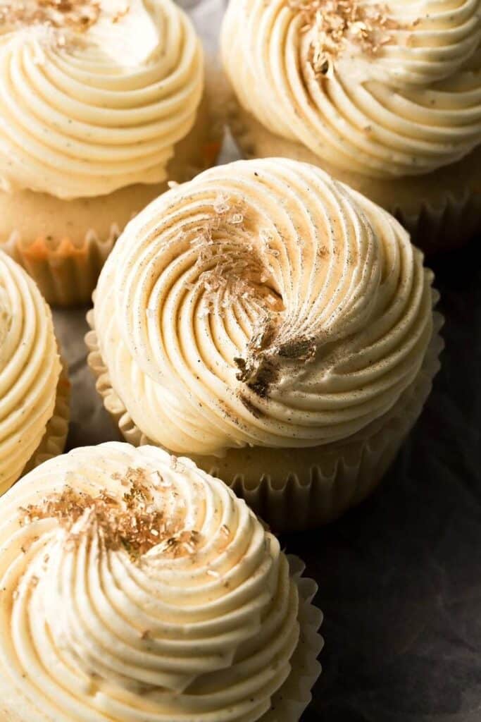 Vanilla cupcakes with swirled buttercream frosting and edible gold flakes, perfect for a luxurious dessert treat.