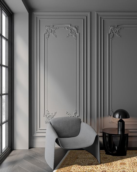 Elegant gray room with ornate wall paneling, modern chair, round table, and black lamp near a large window.