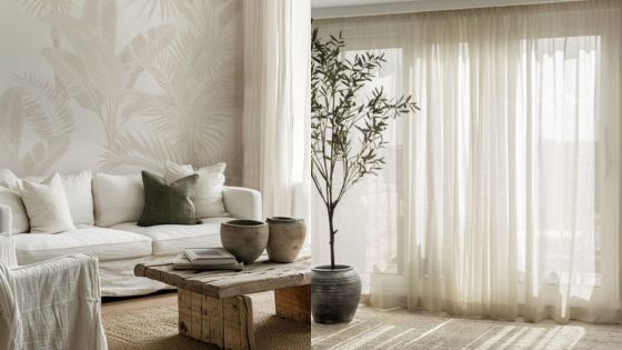 Minimalist living room with white sofa, wood table, potted plant, and sheer curtains. Cozy and serene interior design.