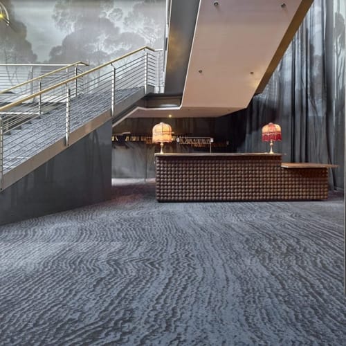 Modern hotel lobby with elegant staircase and stylish reception area, featuring textured carpeting and unique lighting.