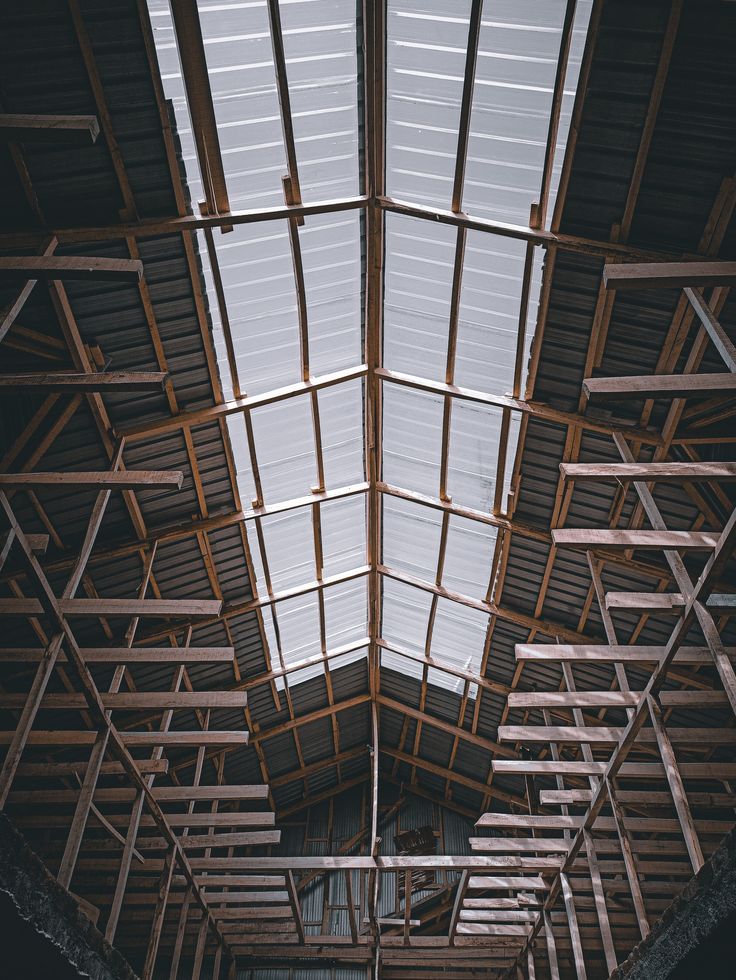 Warehouse roof structure with wooden beams and metal sheets, viewed from below, highlighting architectural design.