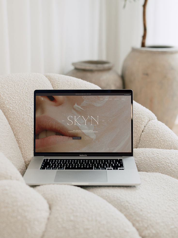 Laptop displaying skincare website Skyn on a cozy chair for a relaxing setting.