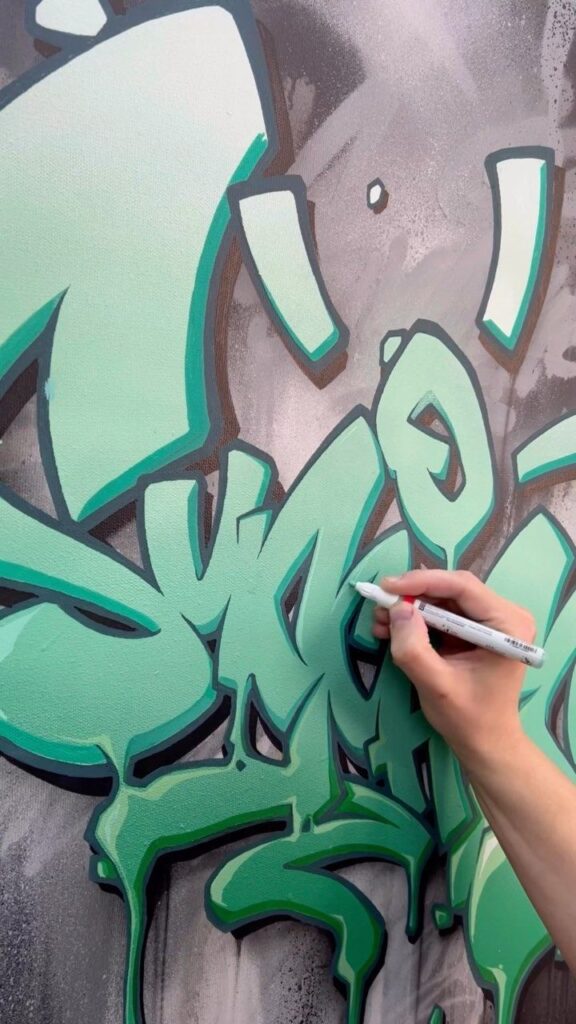 Artist adding detail to vibrant green graffiti on wall with a marker.