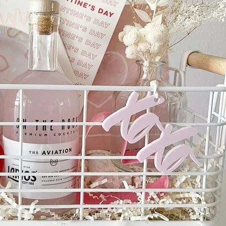 Valentine's Day gift basket with pink drinks, flowers, and XOXO decor in a white wire basket.