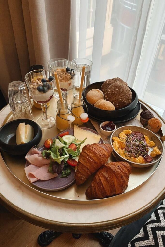 Delicious breakfast spread with croissants, scrambled eggs, salad, yogurt parfaits, and juice on a round table.