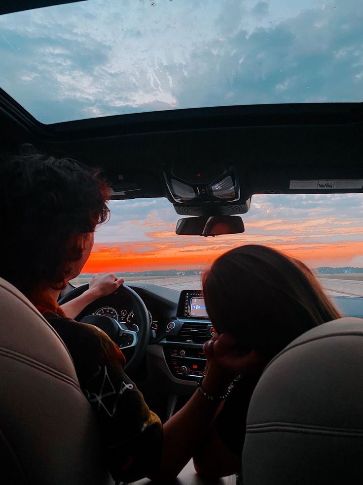 Couple driving at sunset with scenic view through car window, enjoying a serene road trip adventure.