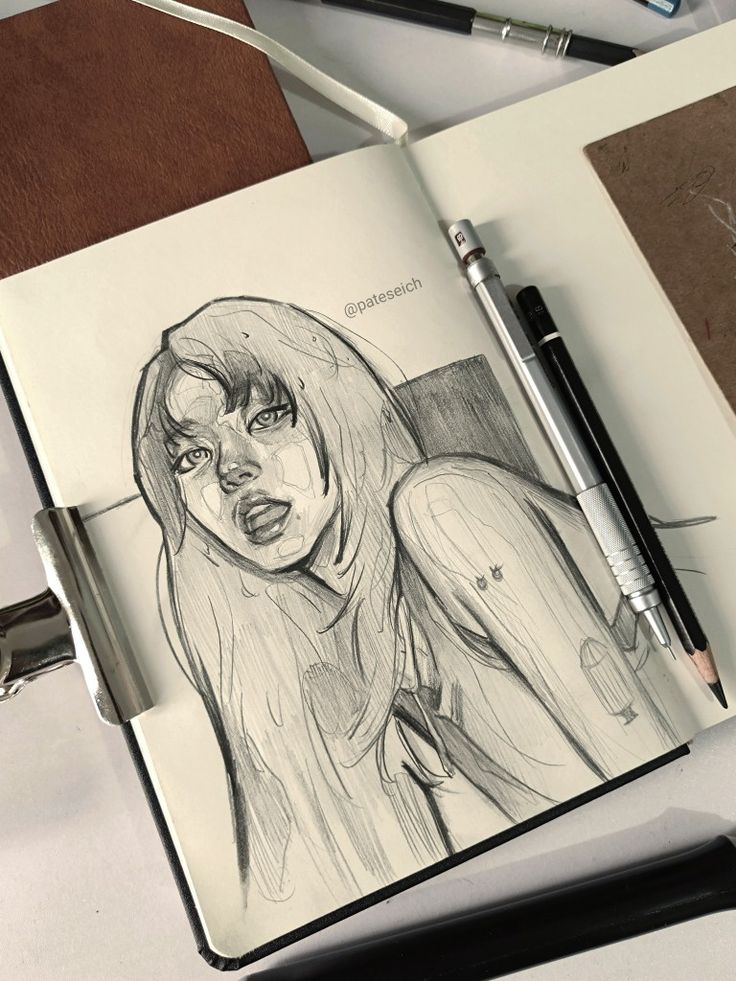 Sketch of a woman in a notebook, surrounded by pencils and an eraser on a desk.