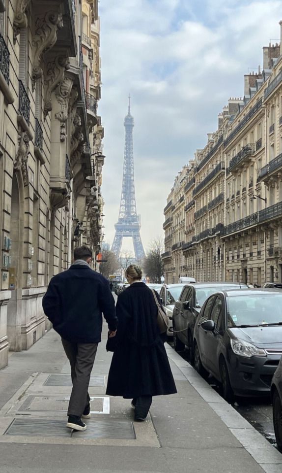 Couple walks down Paris street with Eiffel Tower in background, surrounded by classic European architecture.