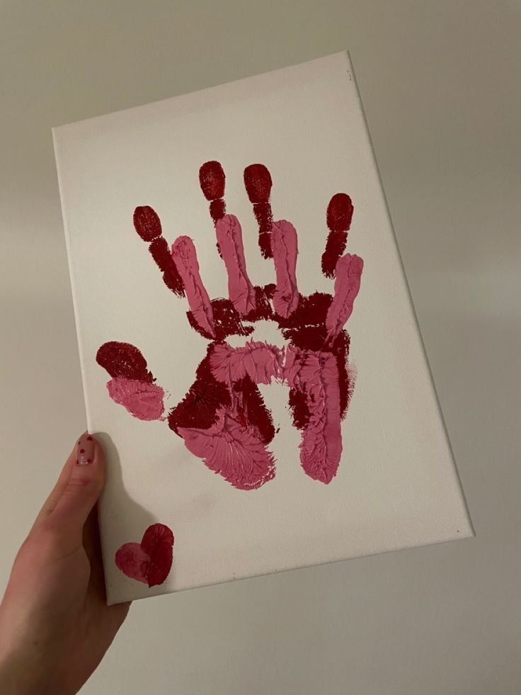 Hand holding canvas with layered red and pink handprints and a heart, symbolizing love and connection.