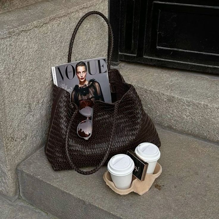 Stylish handbag with magazine and sunglasses, near two takeaway coffee cups on steps.