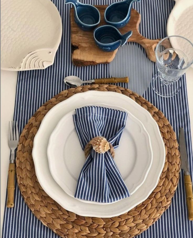 Elegant dining table setup with striped napkin, white plates, and woven placemat on blue and white striped tablecloth.