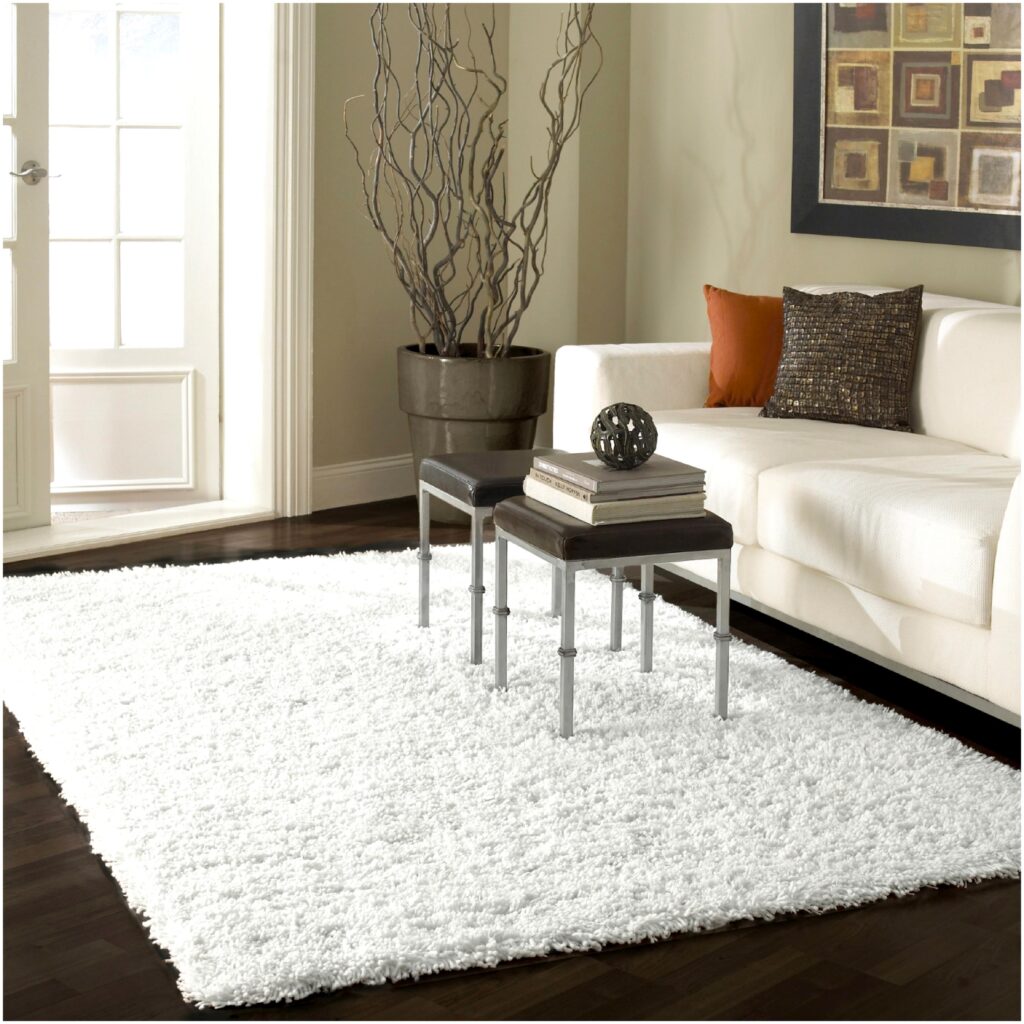 Modern living room with white shag rug, white sofa, two nested tables, abstract art, and a potted plant by the door.