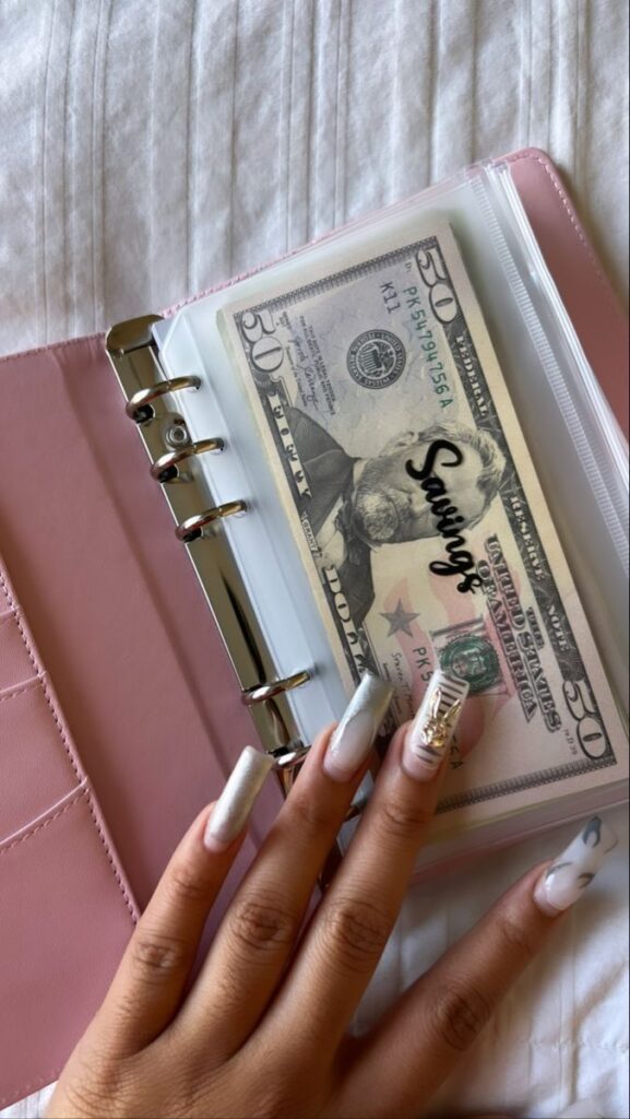 Person with manicured nails holding a binder containing a  bill labeled Savings on a bed.