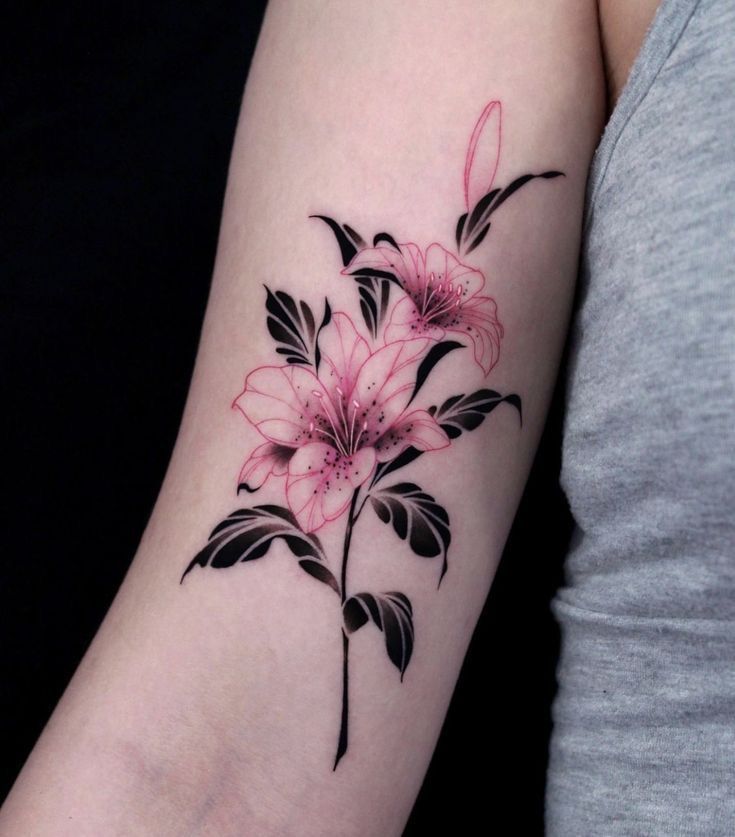 Pink and black floral tattoo on arm with delicate lilies and leaves, showcasing intricate design and artistry.