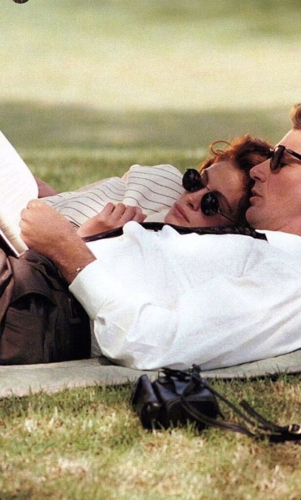 Couple relaxing on grass, reading and wearing sunglasses, enjoying a sunny day in the park.