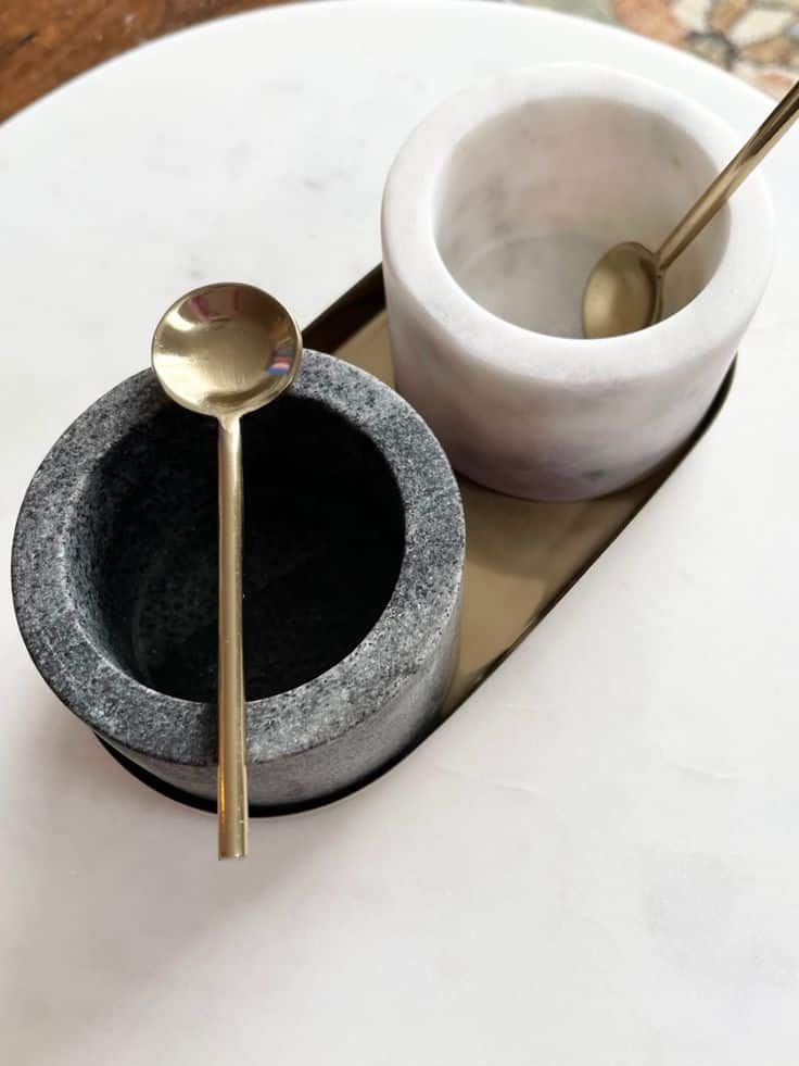 Marble salt and pepper cellars with brass spoons on a white counter. Elegant kitchen accessory for seasoning.