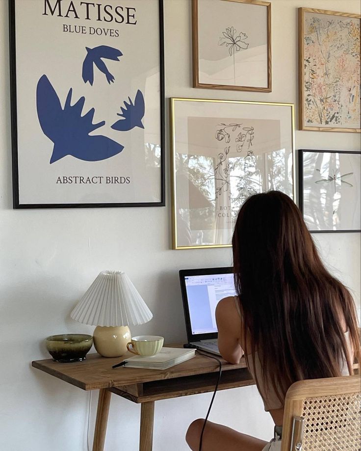 Person working at home office desk with art and laptop. Cozy workspace interior with a gallery wall display.