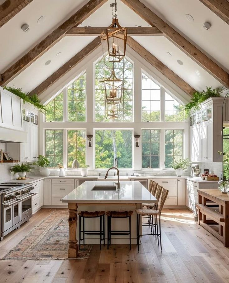 Spacious kitchen with vaulted ceiling, large windows, wooden beams, white cabinets, and island with bar stools.