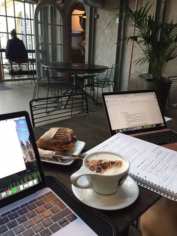 Cozy cafe workspace with laptops, a cappuccino, and a sandwich, creating a productive atmosphere.